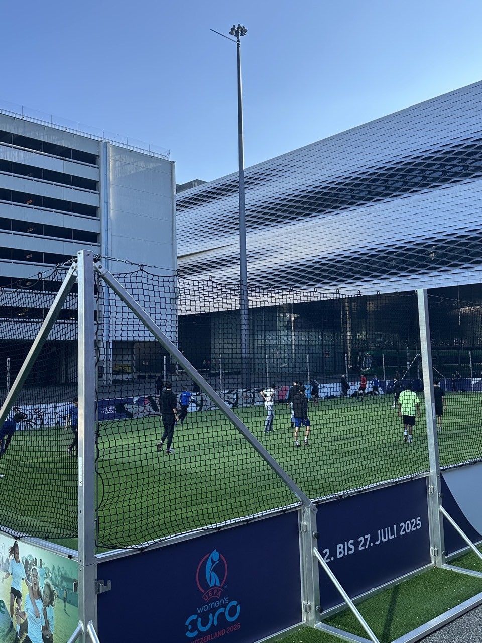 フェンスで囲まれた人工芝のミニピッチでサッカーを楽しむ人々